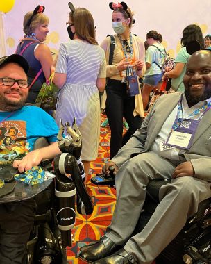 disability community | SMA News Today | Kevin Schaefer and LaMondre Pough sit side-by-side in their wheelchairs at the 2022 Cure SMA conference in Anaheim, California.