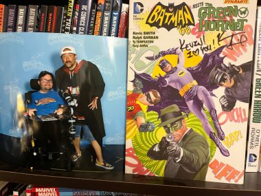 living with SMA | SMA News Today | A photo of columnist Kevin Schaefer with writer and filmmaker Kevin Smith sits on a shelf next to a Batman and Green Hornet comic book signed by Smith.