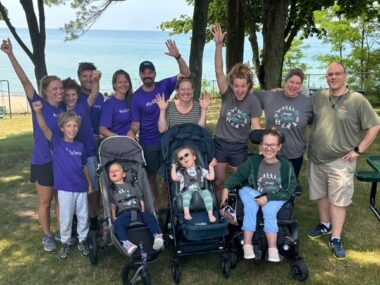 A group of people, outside, cheer and wave at the camera.
