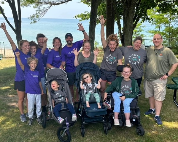 A group of people, outside, cheer and wave at the camera.