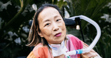 Advocacy activist Alice Wong sits in her wheelchair, with plants in the background.
