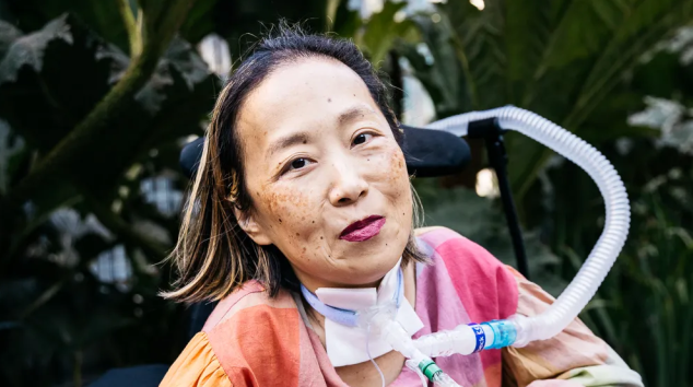 Advocacy activist Alice Wong sits in her wheelchair, with plants in the background.