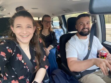 Three people smile for a photo inside a van. The author is sitting in the middle of the back row, while two of her friends sit in the driver and passenger seats.