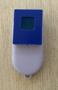 Something that looks like a large gray computer mouse with a blue surface over half of it sits on a tan surface.