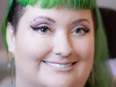 A headshot, seen close up, shows a woman with black and green hair.