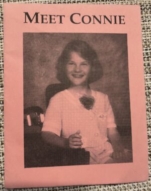 A photocopied pink booklet shows a young girl smiling while grasping the joystick of her wheelchair.