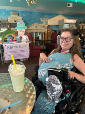 A woman sits in a colorful coffee shop with a large milkshake sitting on a table in front of her.